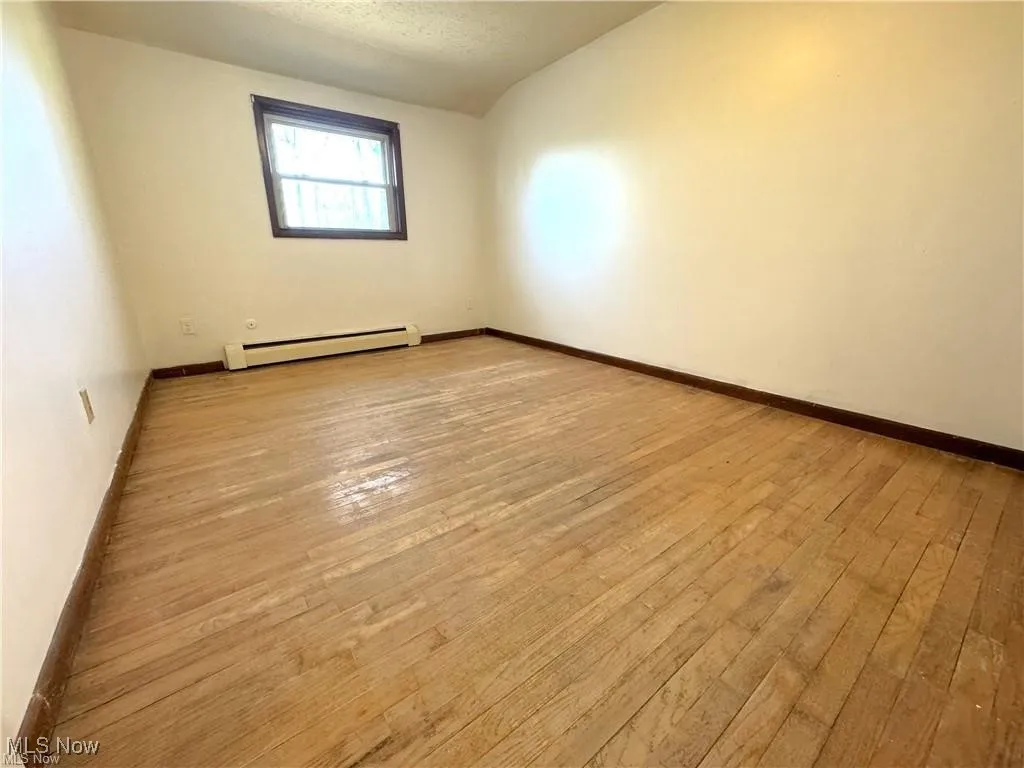 Spare room featuring lofted ceiling, a baseboard radiator, hardwood / wood-style floors, and a textured ceiling