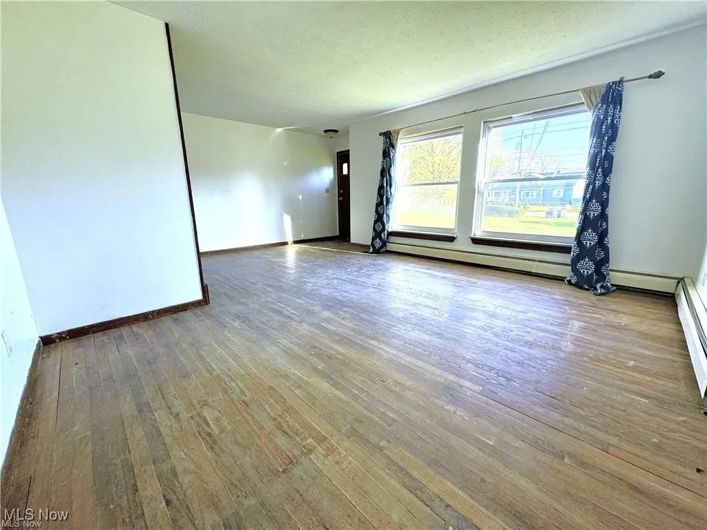 Unfurnished room featuring hardwood / wood-style floors, a textured ceiling, and a baseboard radiator