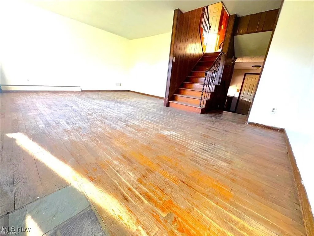 Unfurnished living room with hardwood / wood-style floors, stairway, and a baseboard radiator