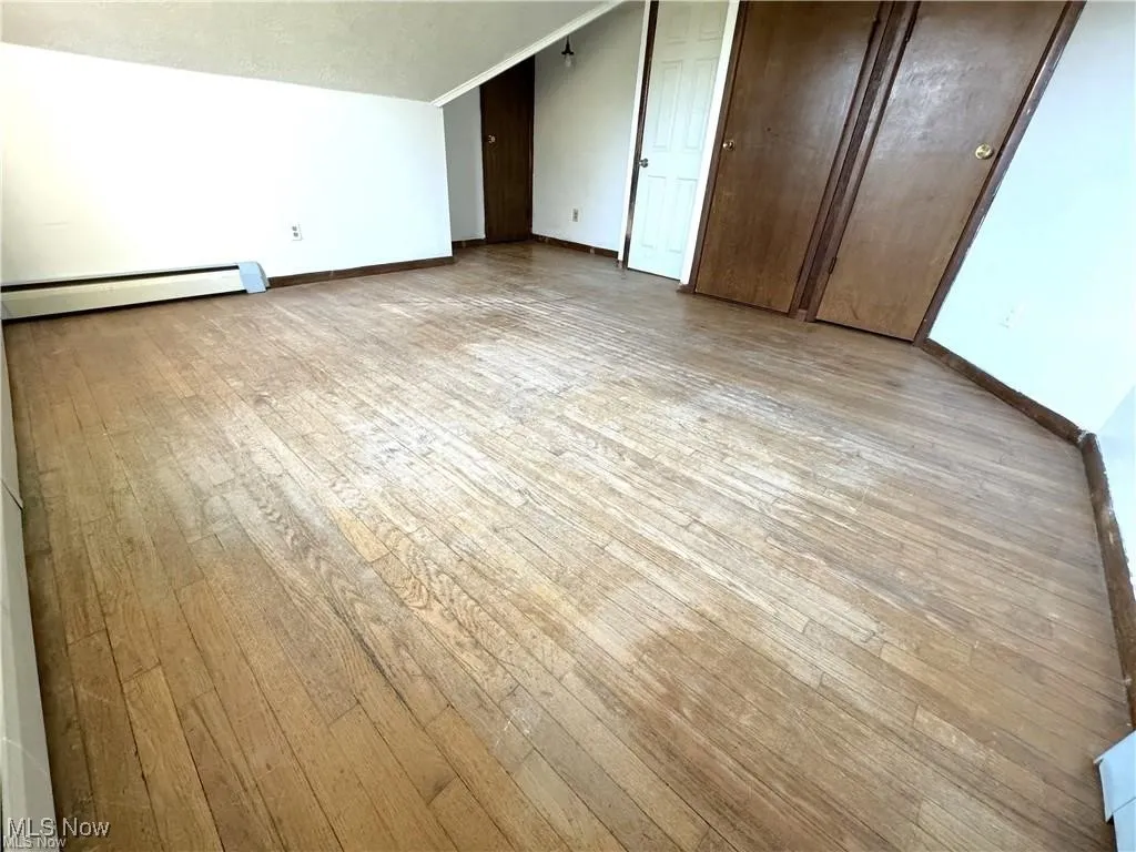 Bonus room featuring a baseboard radiator, light wood-style flooring, and vaulted ceiling