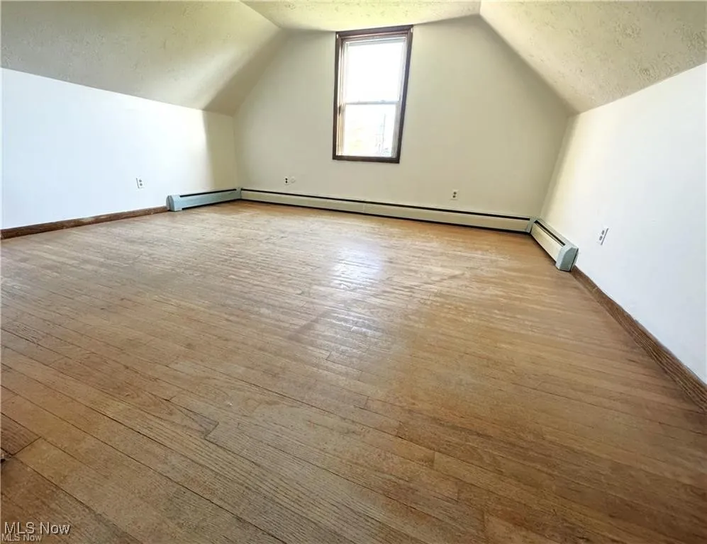 Bonus room featuring a textured ceiling, lofted ceiling, and wood finished floors