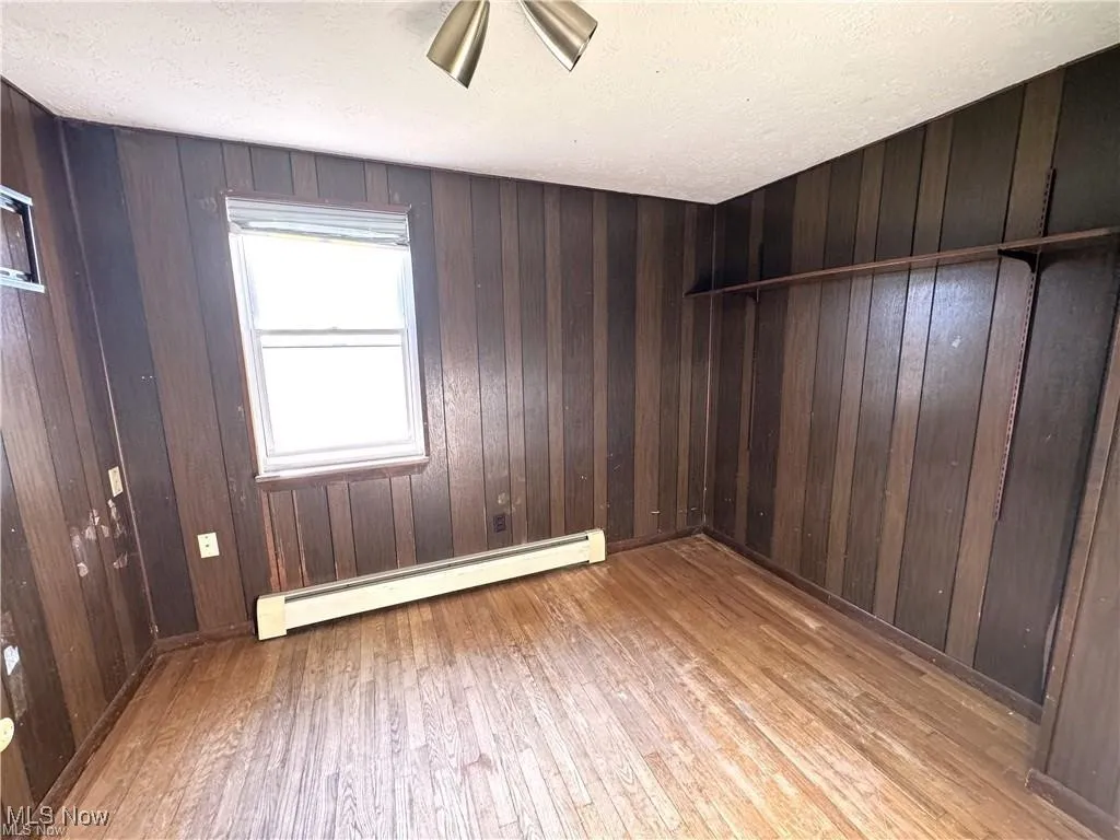 Spare room with a baseboard heating unit, wood walls, a textured ceiling, and wood-type flooring
