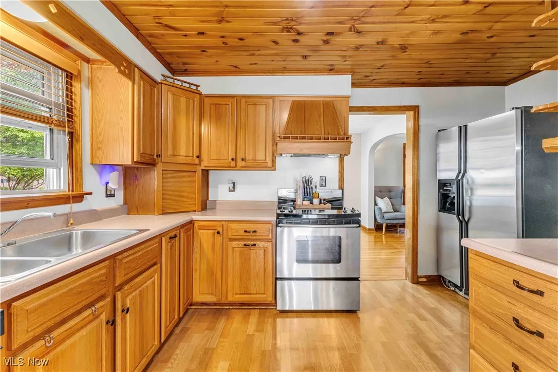 Kitchen featuring appliances with stainless steel finishes, light wood-style flooring, custom range hood, light countertops, and wooden ceiling