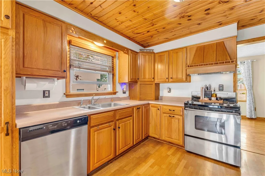 Kitchen featuring appliances with stainless steel finishes, light wood finished floors, custom exhaust hood, wooden ceiling, and light countertops