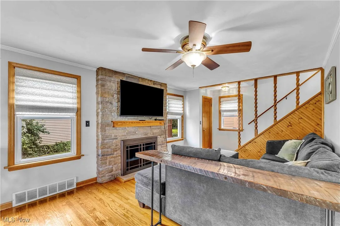 Living room featuring crown molding, light wood-style floors, a fireplace, a ceiling fan, and stairs