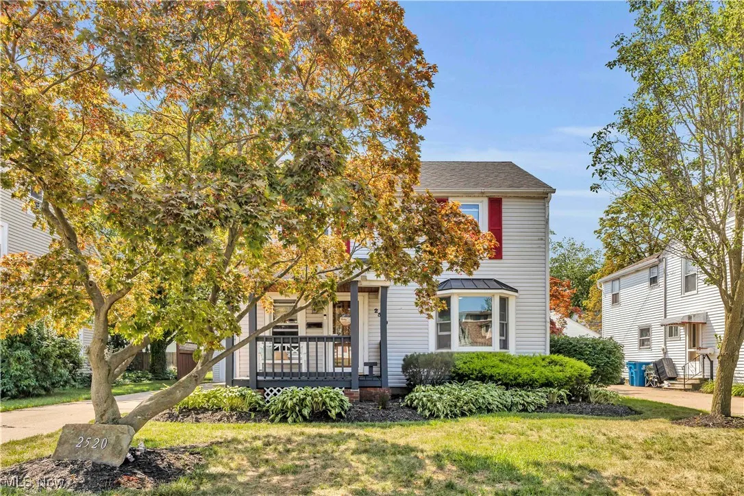 View of property hidden behind natural elements featuring a front lawn and a porch