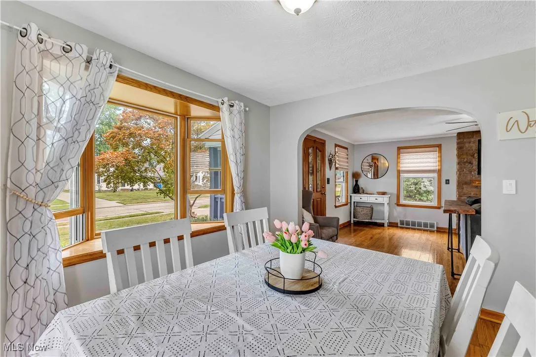 Dining space with arched walkways, wood finished floors, a textured ceiling, and ornamental molding
