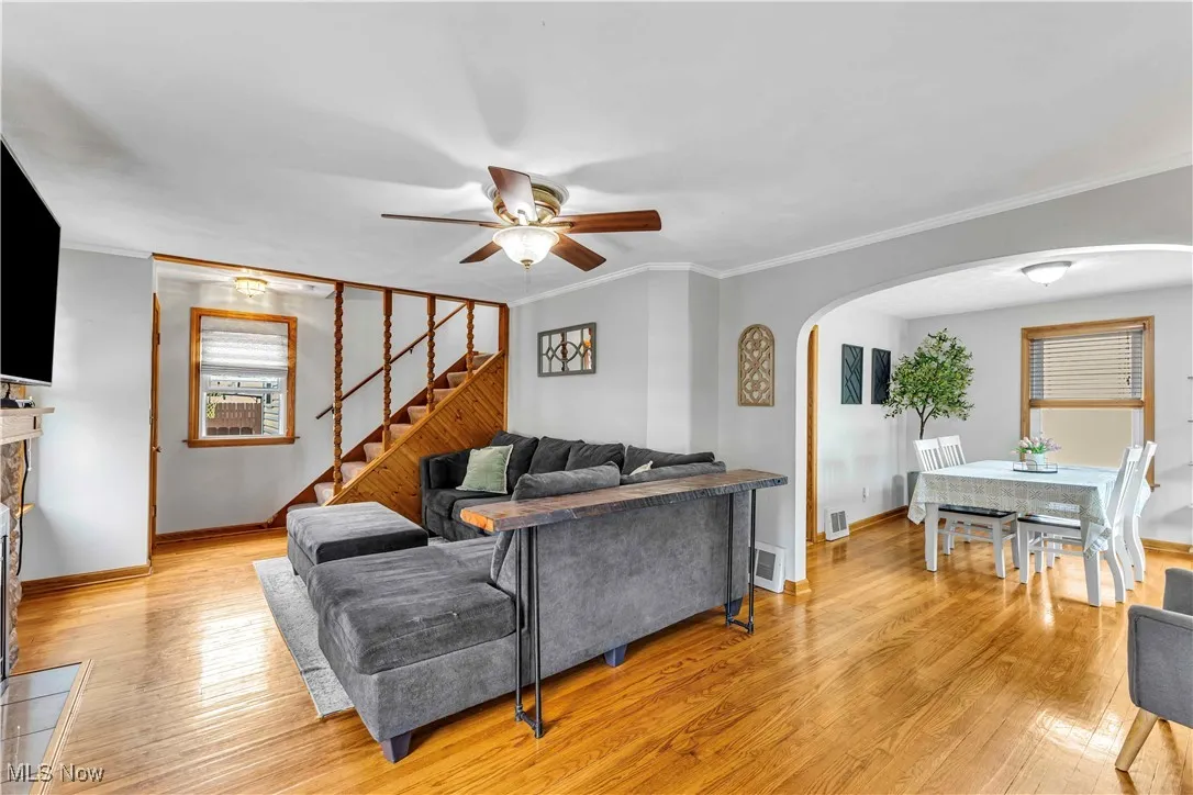 Living area with crown molding, light wood finished floors, stairway, a ceiling fan, and arched walkways