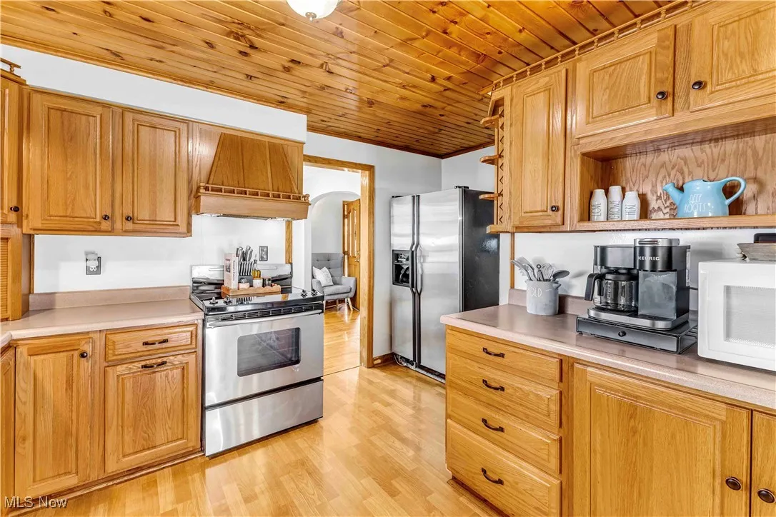Kitchen featuring stainless steel appliances, light wood-style flooring, custom range hood, light countertops, and wood ceiling