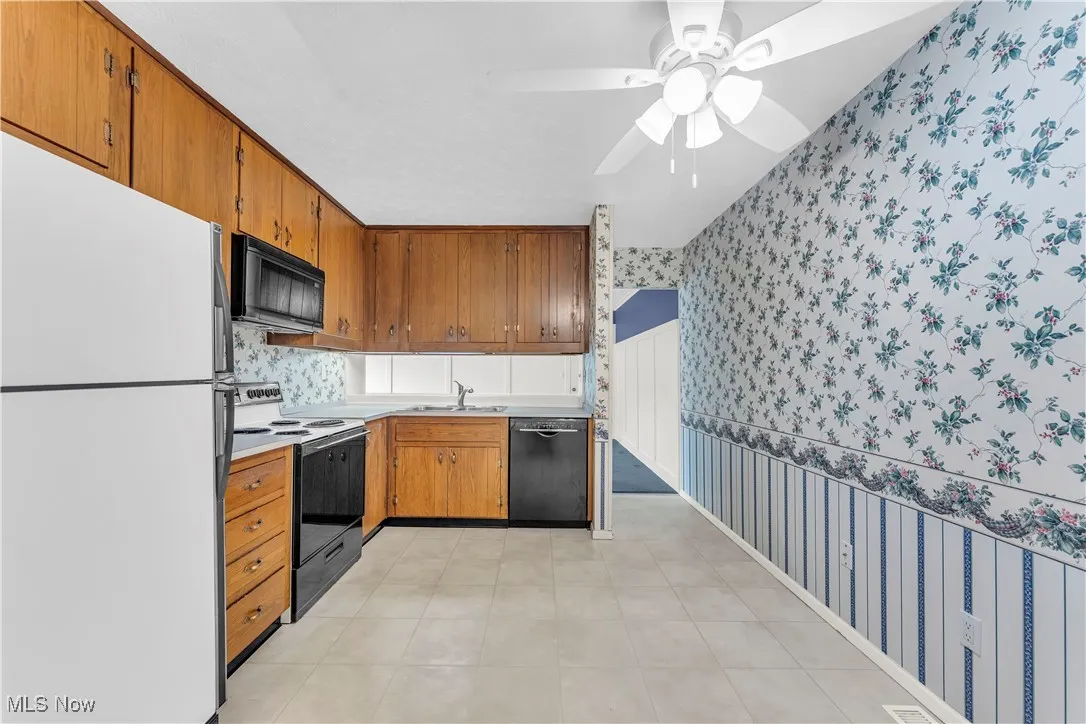 Kitchen with black appliances, wallpapered walls, brown cabinets, ceiling fan, and light countertops