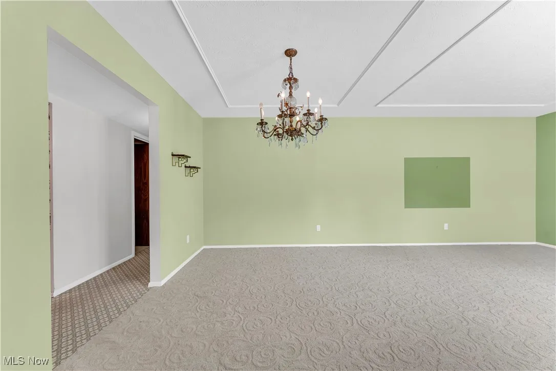 Carpeted spare room featuring a chandelier and baseboards