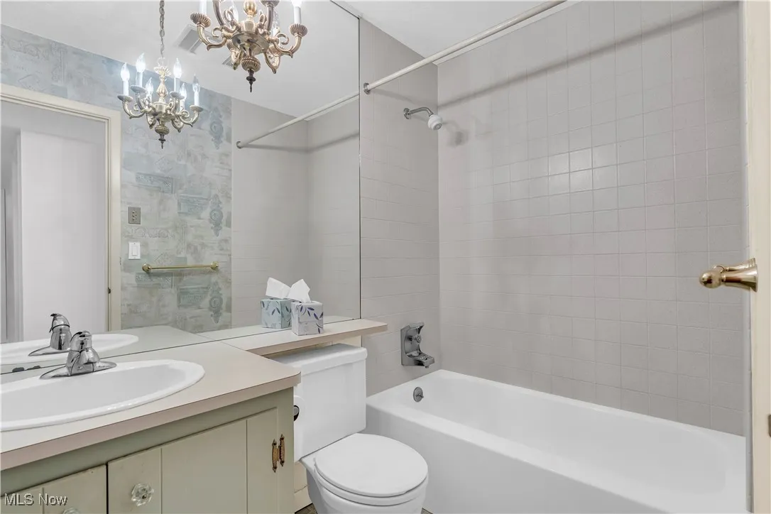 Bathroom featuring a chandelier, vanity, bathtub / shower combination, and wallpapered walls