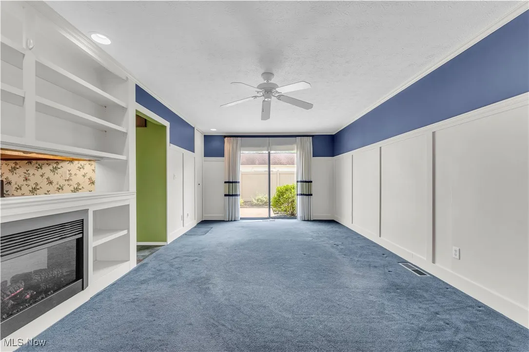 Unfurnished living room with a decorative wall, built in features, ceiling fan, a wainscoted wall, and carpet floors