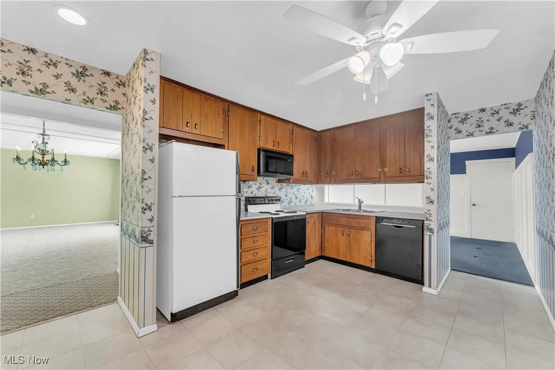 Kitchen featuring light carpet, black appliances, brown cabinets, and wallpapered walls