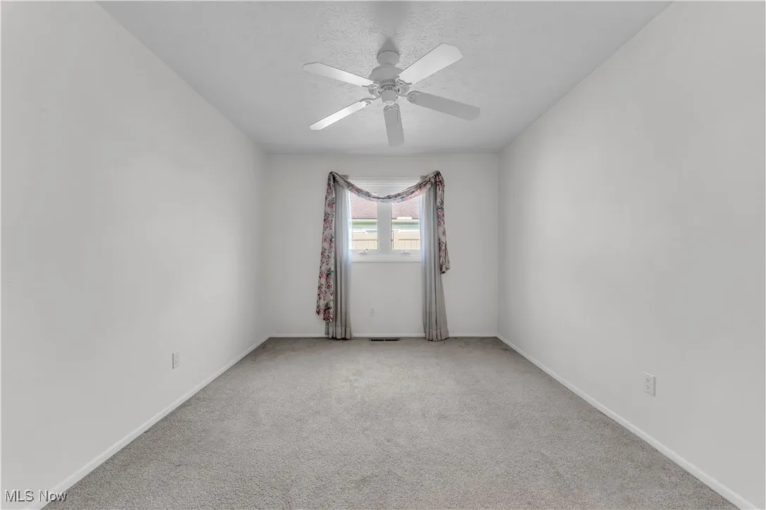 Unfurnished room featuring light colored carpet, a ceiling fan, and a textured ceiling