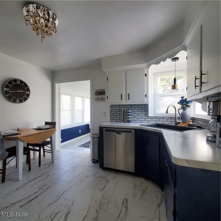 Kitchen featuring light marble finish flooring, light countertops, dishwasher, decorative backsplash, and healthy amount of natural light