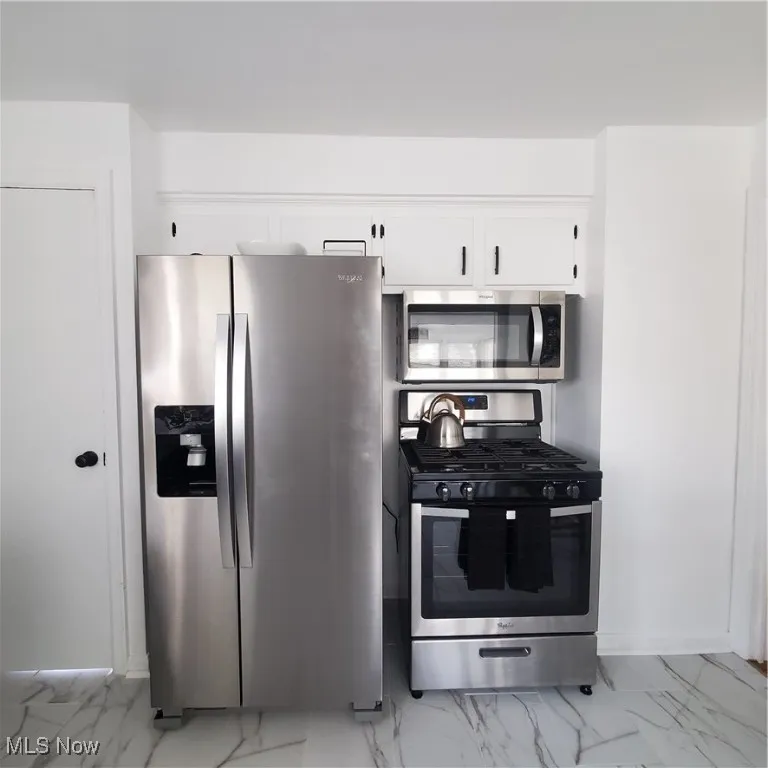 Kitchen featuring range, light marble finish flooring, refrigerator, and white cabinets