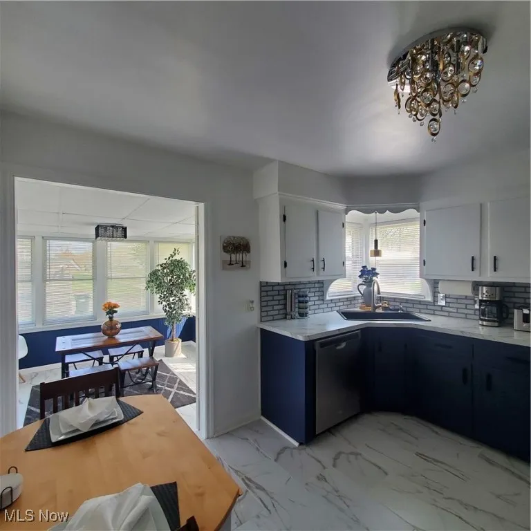 Kitchen featuring tasteful backsplash, light marble finish floors, light countertops, dishwasher, and white cabinetry