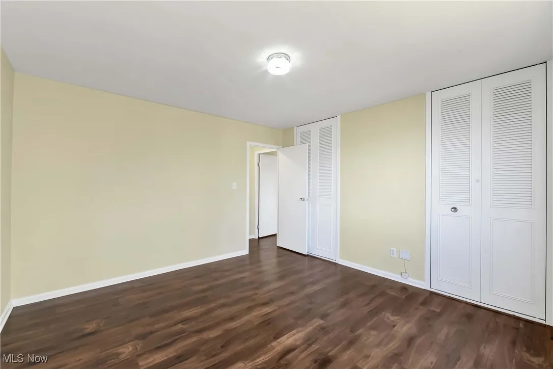 Unfurnished bedroom featuring dark wood finished floors, two closets, and baseboards