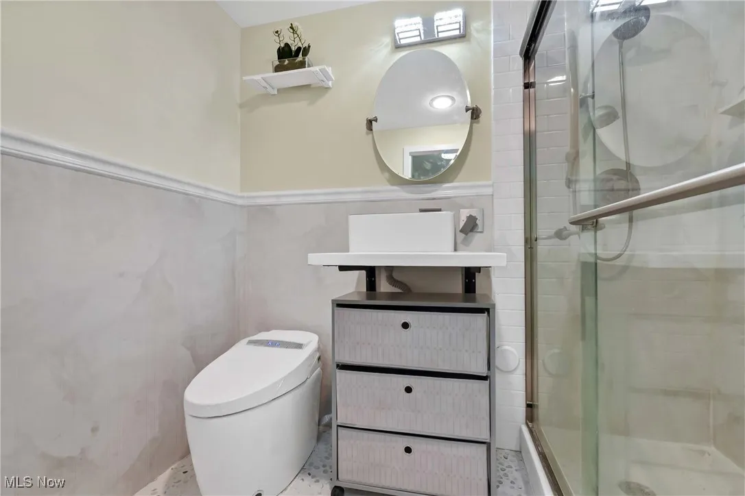 Bathroom featuring toilet, tile walls, wainscoting, a shower stall, and vanity