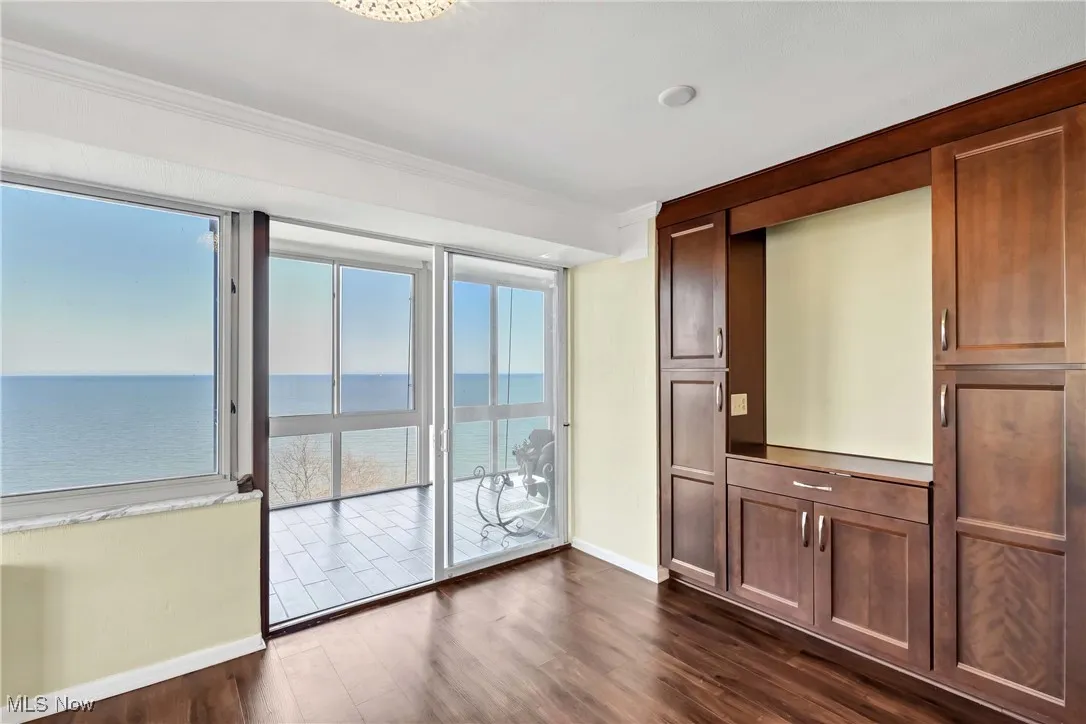 Unfurnished room featuring dark wood finished floors, baseboards, a water view, and ornamental molding