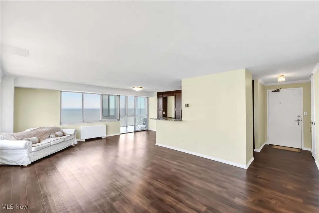 Unfurnished living room featuring baseboards, dark wood-style floors, and radiator heating unit