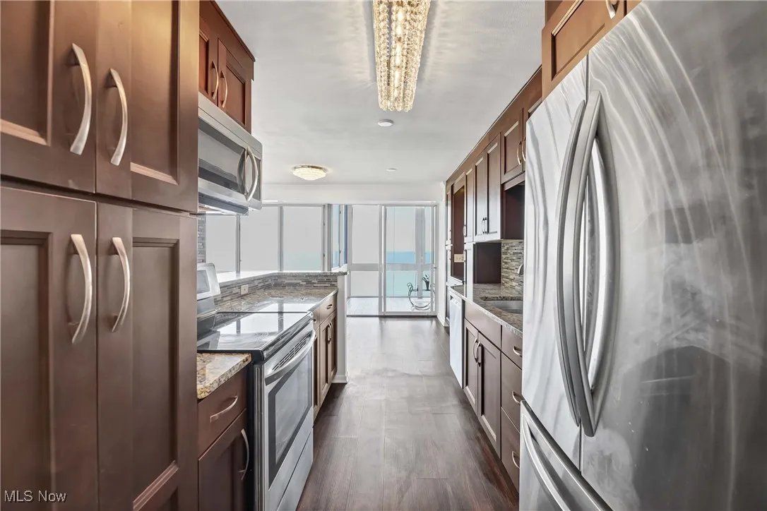 Kitchen featuring decorative backsplash, light stone counters, a notable chandelier, and stainless steel appliances
