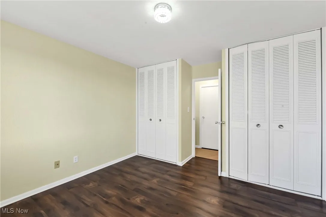Unfurnished bedroom featuring dark wood-style floors, baseboards, and multiple closets
