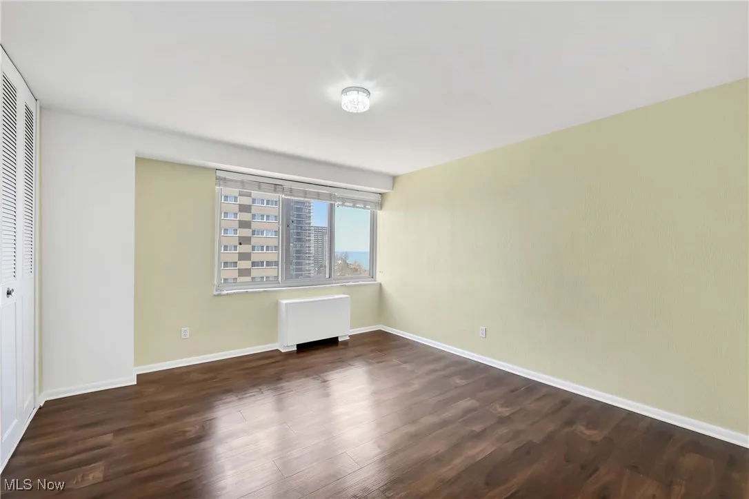 Unfurnished bedroom with radiator, wood finished floors, a closet, and baseboards