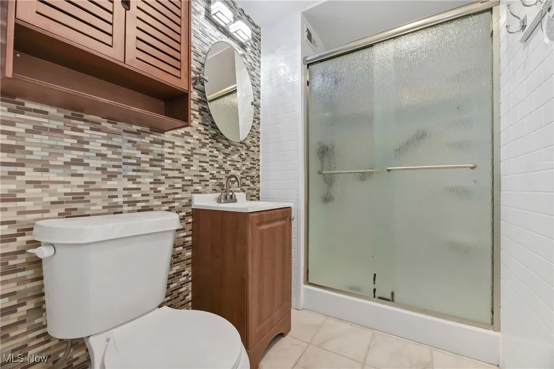 Bathroom featuring a shower stall, tile walls, toilet, tile patterned floors, and vanity