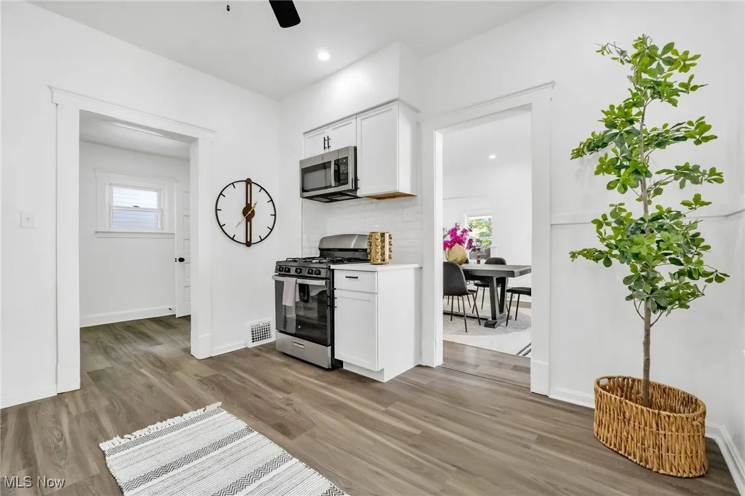 Kitchen with appliances with stainless steel finishes, wood finished floors, a ceiling fan, white cabinetry, and tasteful backsplash