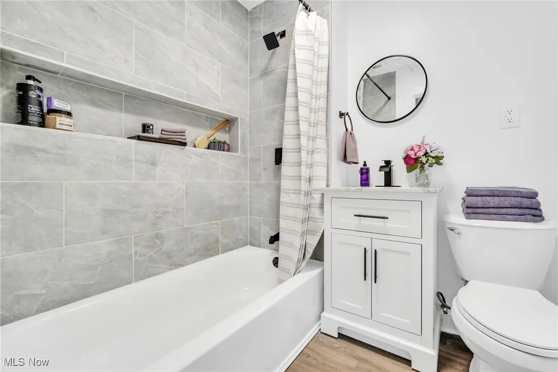Bathroom featuring wood finished floors, shower / bath combo with shower curtain, and vanity