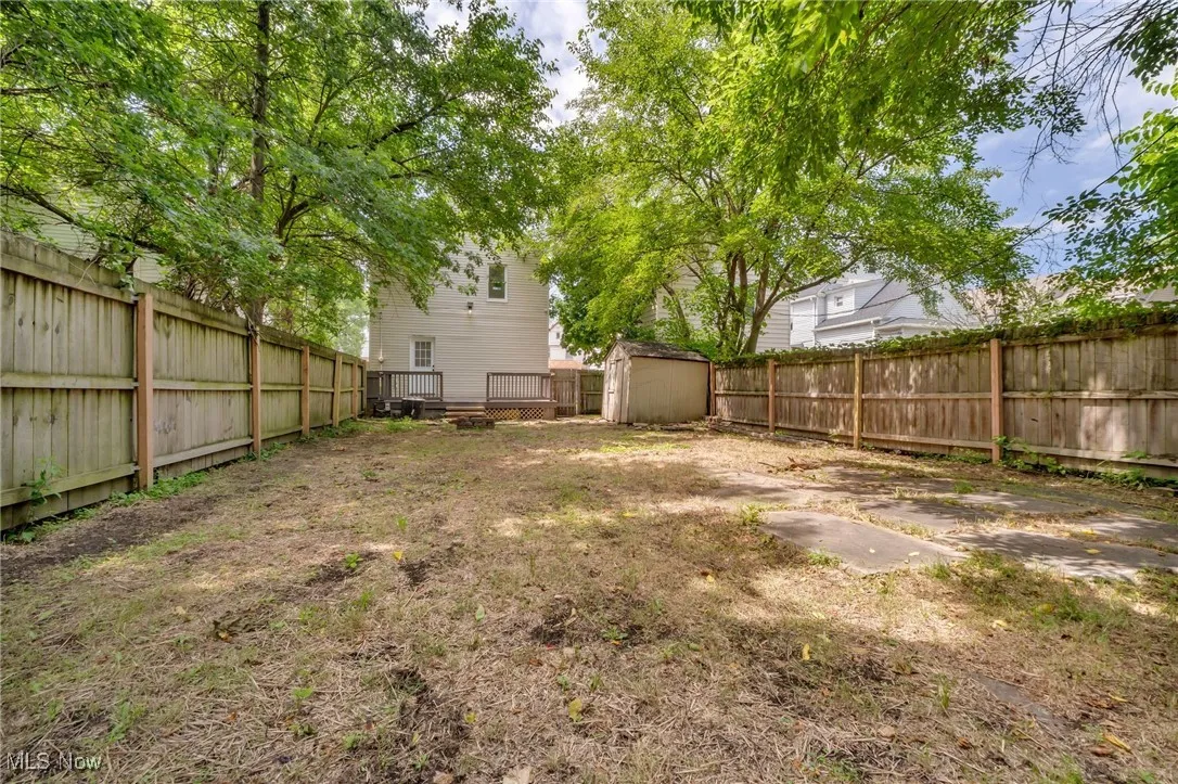 Fenced backyard featuring a storage unit and a wooden deck