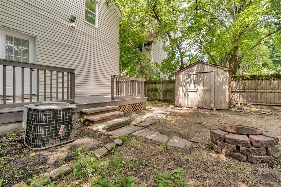 Fenced backyard featuring an outdoor fire pit, a storage shed, and a deck