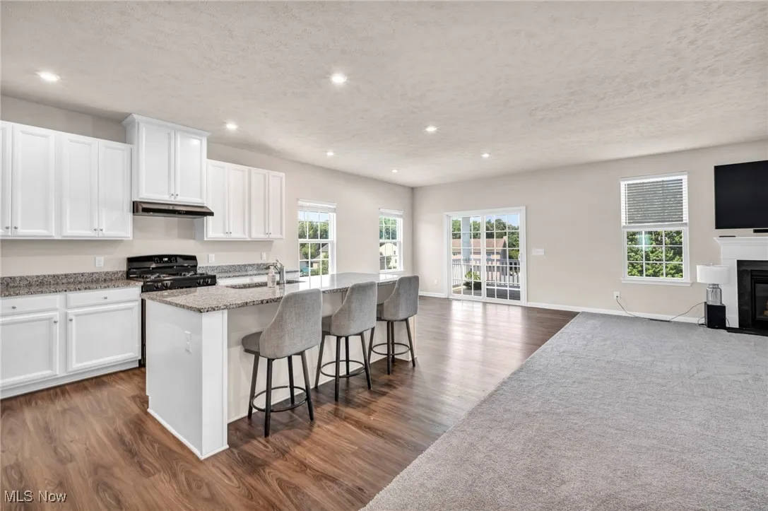 Kitchen with open floor plan, a fireplace with flush hearth, a textured ceiling, an island with sink, and white cabinetry
