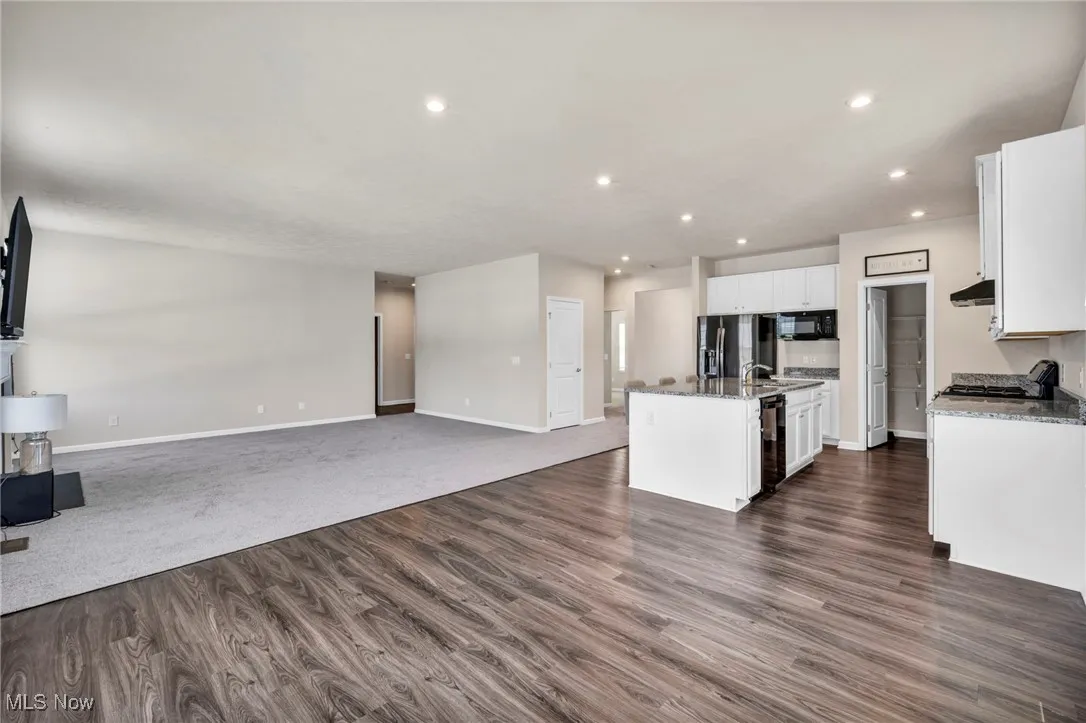 Kitchen with open floor plan, white cabinets, an island with sink, recessed lighting, and stainless steel appliances