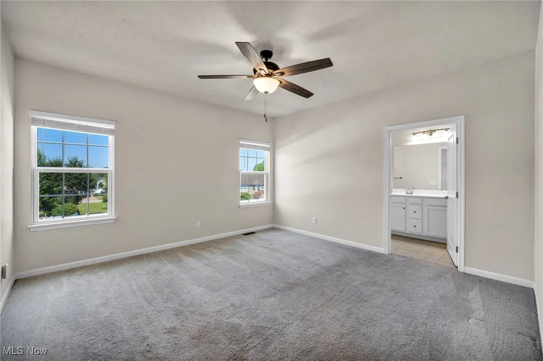 Unfurnished bedroom featuring light carpet, connected bathroom, and ceiling fan