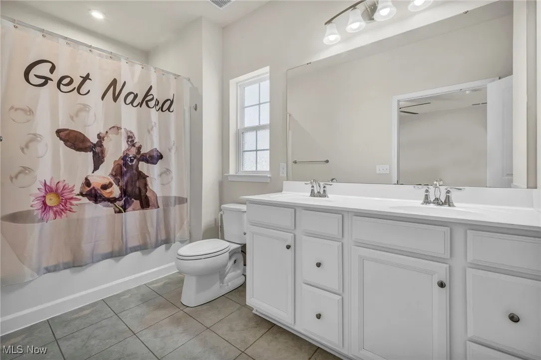 Full bathroom with double vanity, tile patterned floors, and shower / bath combo
