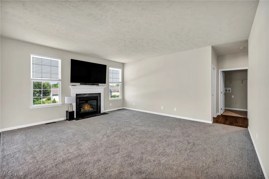 Unfurnished living room featuring neutral colored carpet, a textured ceiling, and a fireplace with flush hearth