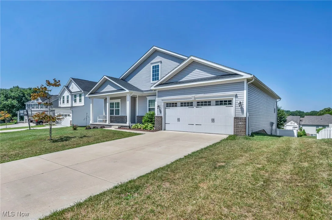 View of front of home featuring a front yard, driveway, a garage, covered porch, and brick siding