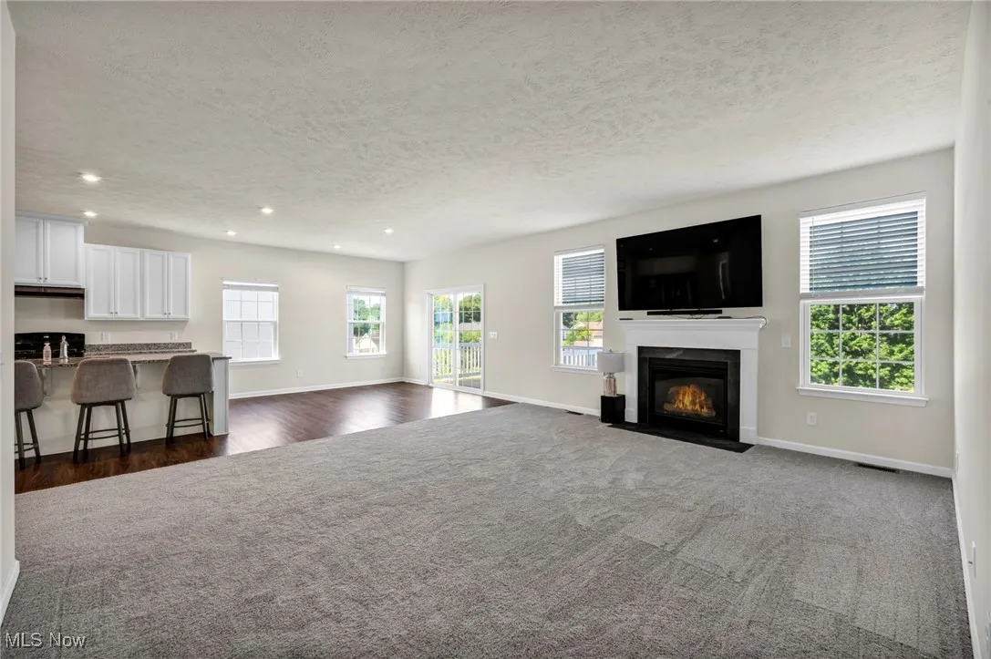 Living area featuring a fireplace with flush hearth, a textured ceiling, neutral carpet, and recessed lighting