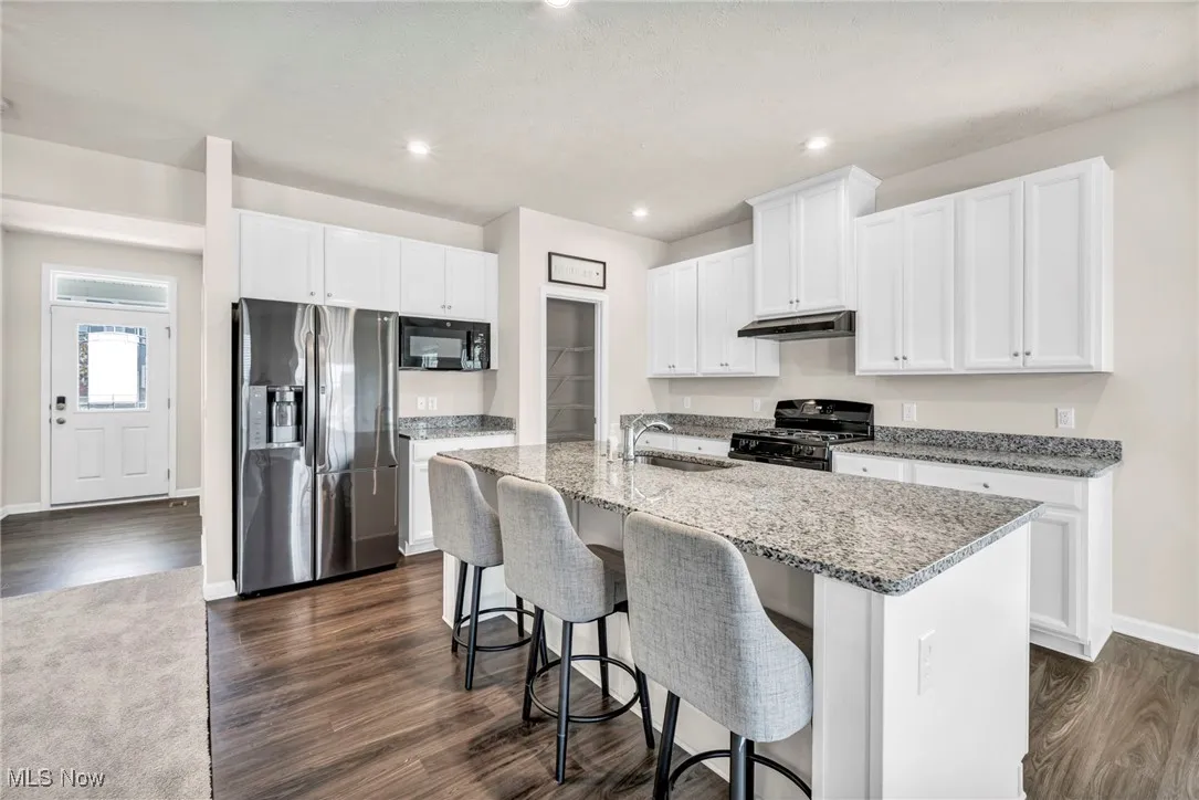 Kitchen with stainless steel appliances, an island with sink, dark wood-type flooring, and recessed lighting