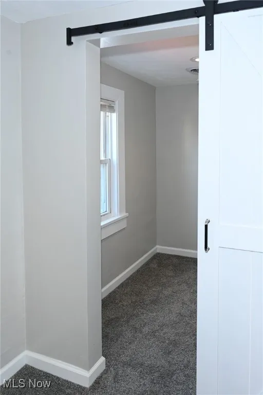Empty room with a barn door and dark colored carpet