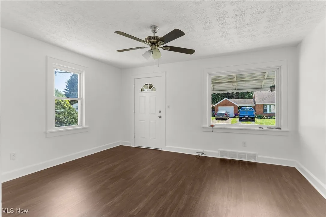 Unfurnished living room with dark wood-type flooring, a textured ceiling, and a ceiling fan