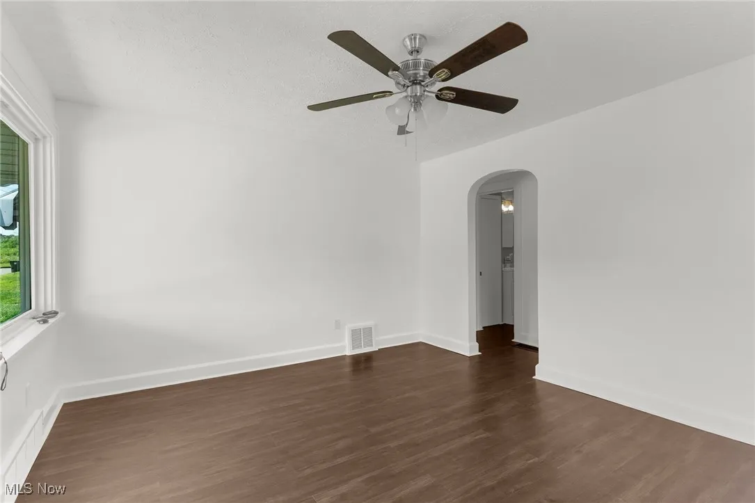 Empty room featuring dark wood-style flooring, a textured ceiling, arched walkways, and a ceiling fan