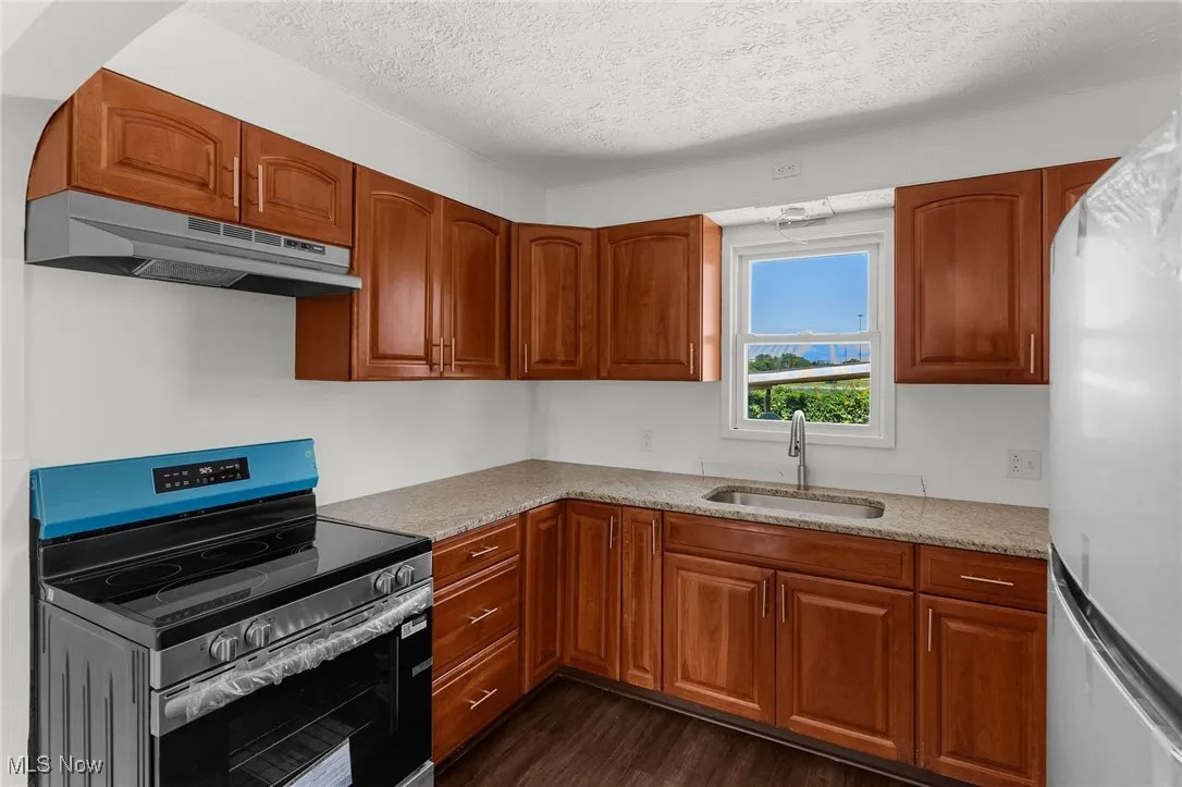Kitchen with stainless steel electric range oven, under cabinet range hood, freestanding refrigerator, a textured ceiling, and dark wood finished floors