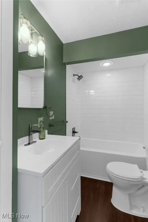 Bathroom with vanity, a textured ceiling, wood finished floors, and bathtub / shower combination