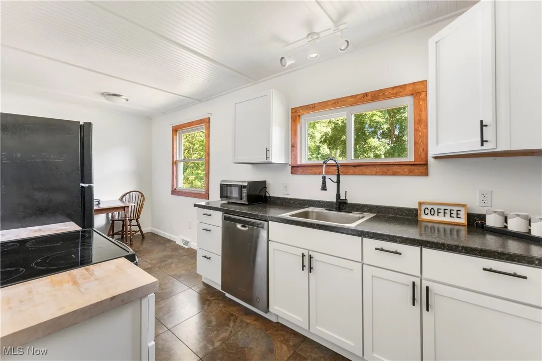 Kitchen featuring freestanding refrigerator, stainless steel dishwasher, white cabinets, and range with electric stovetop