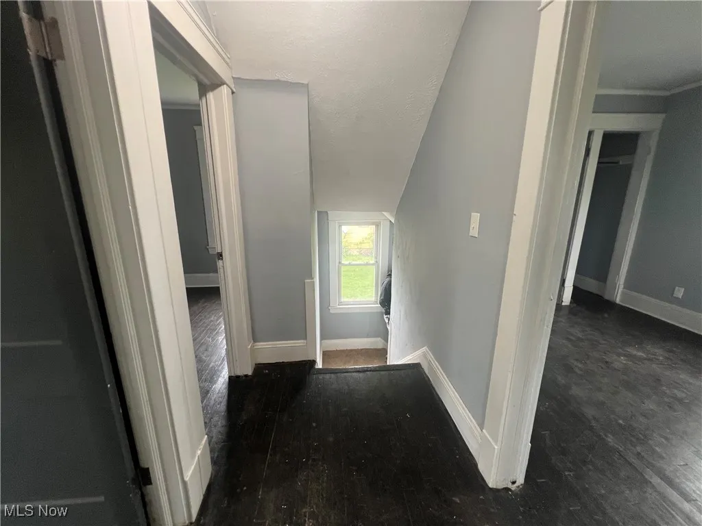 Hallway featuring an upstairs landing, lofted ceiling, wood finished floors, and a textured ceiling