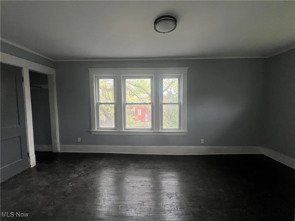 Unfurnished bedroom featuring ornamental molding, dark wood-style flooring, and a closet